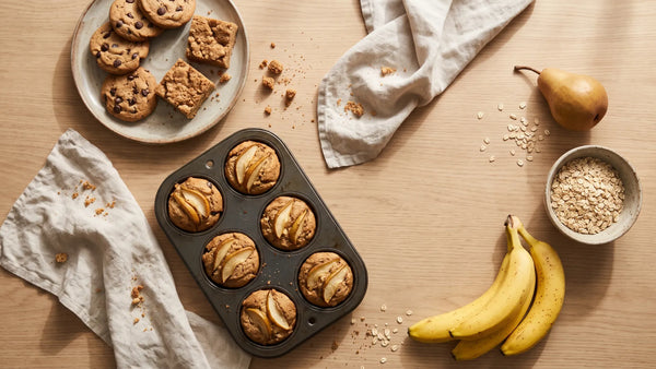 Vegan protein muffins with pear, chocolate chip cookies and blondies on a wooden table with oats, a pear and bananas – baking with protein powder