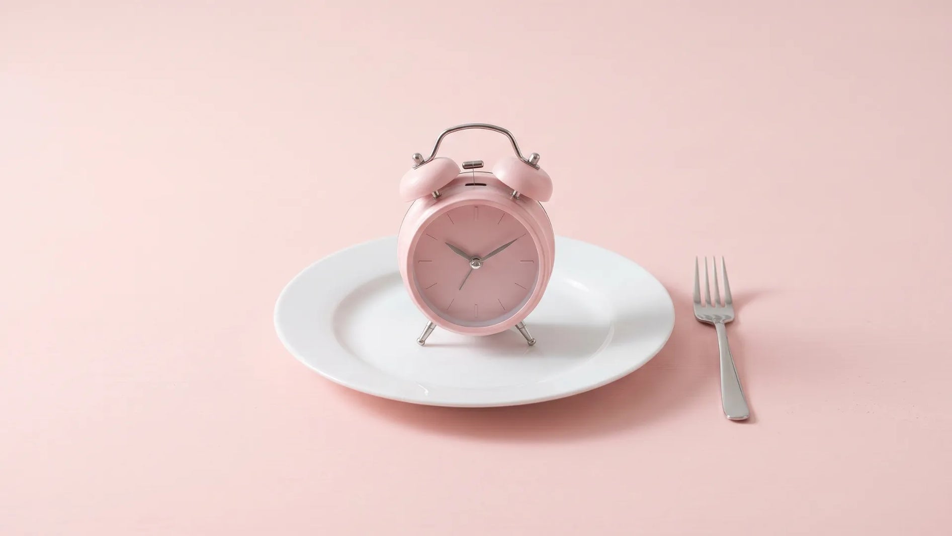 Pink alarm clock on an empty plate with a fork – fasted training for women before breakfast