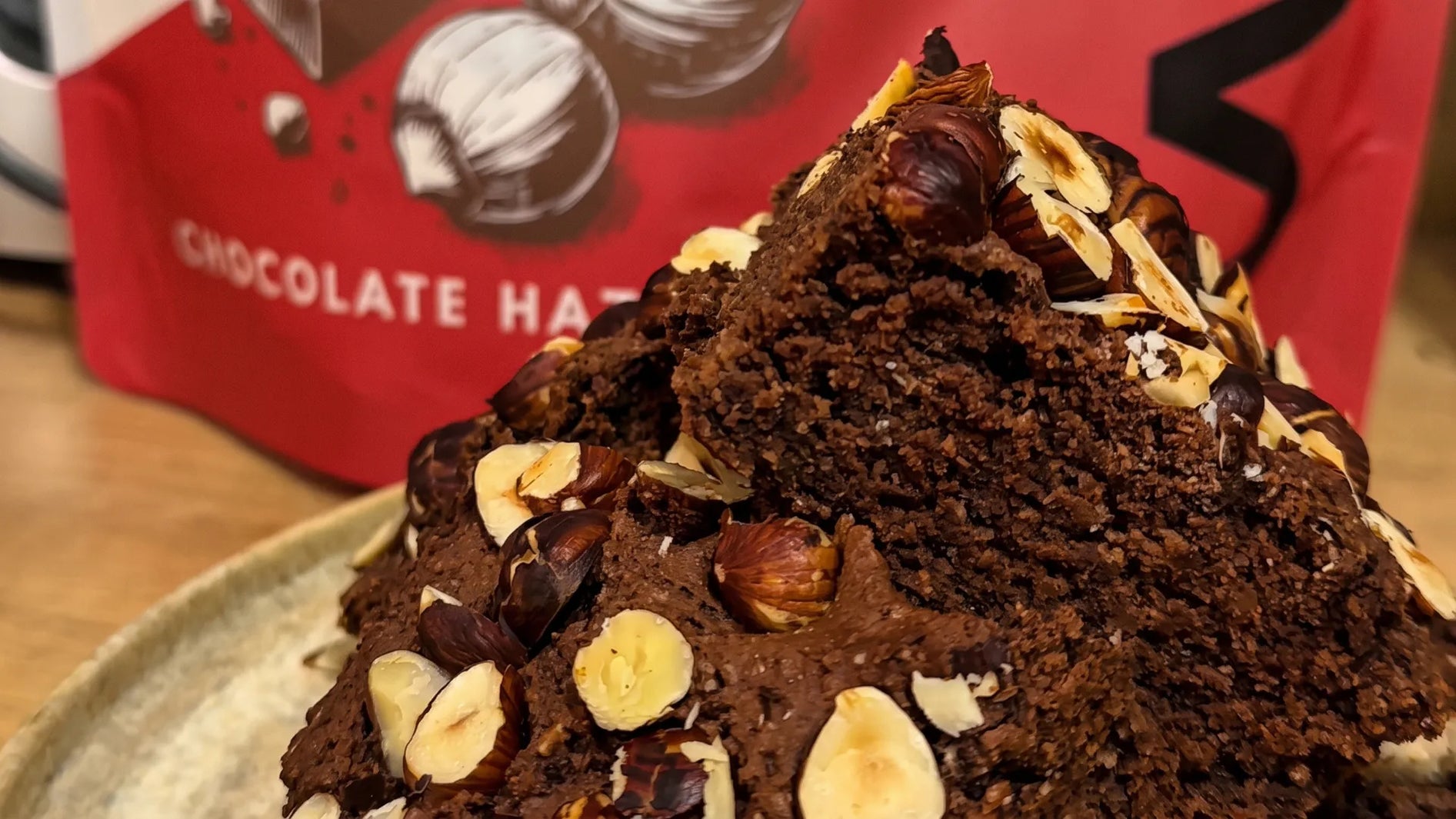 Fudgy vegan protein brownies topped with roasted hazelnuts, in front of a WAM Protein Chocolate Hazelnut pouch