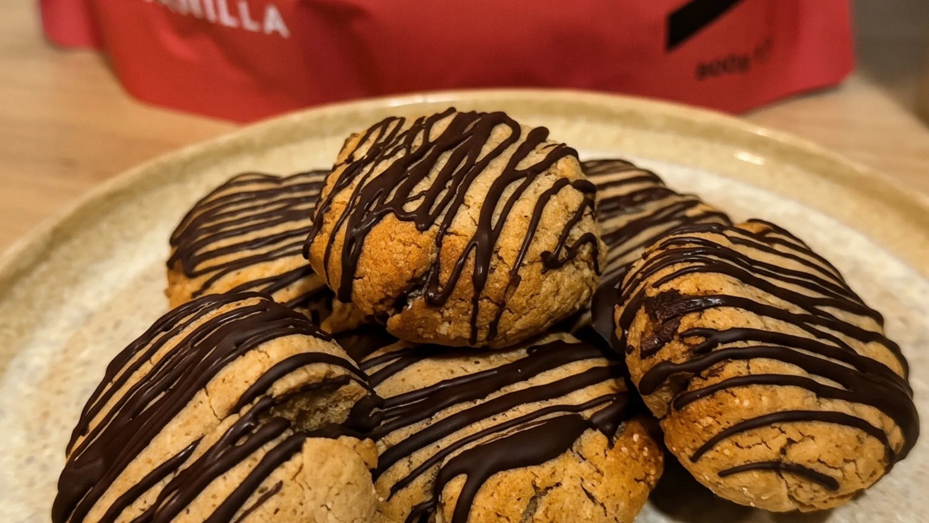Soft vegan gingerbread protein cookies drizzled with dark chocolate on a ceramic plate, in front of a WAM Protein Pure Vanilla pouch