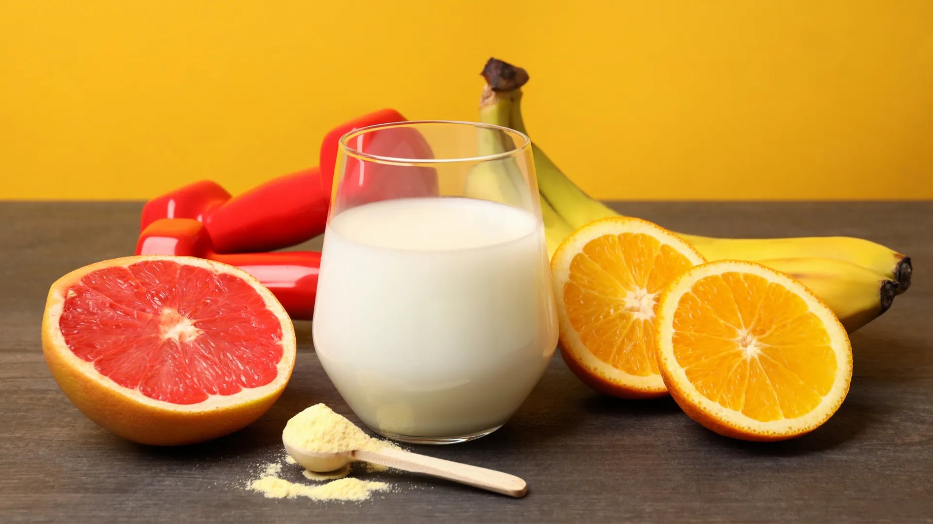 Glass of plant milk with grapefruit, oranges, bananas, a scoop of protein powder and red dumbbells – plant-based nutrition during menopause