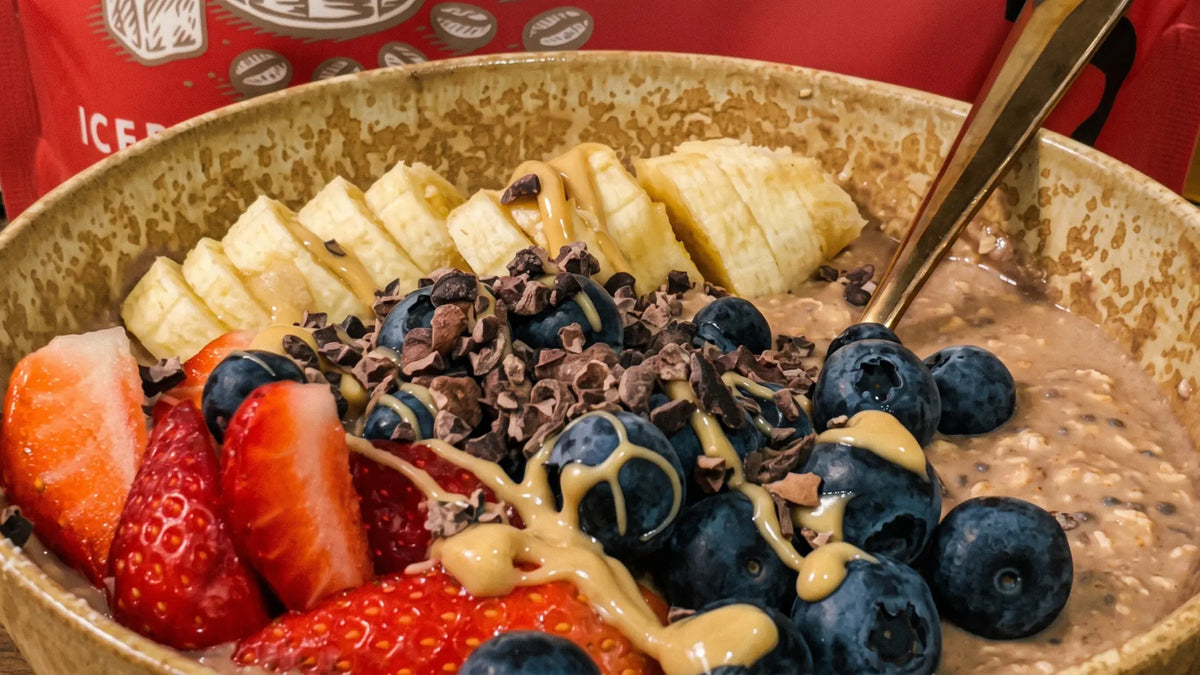 Overnight protein oats topped with banana, strawberries, blueberries, cacao nibs and nut butter in a ceramic bowl